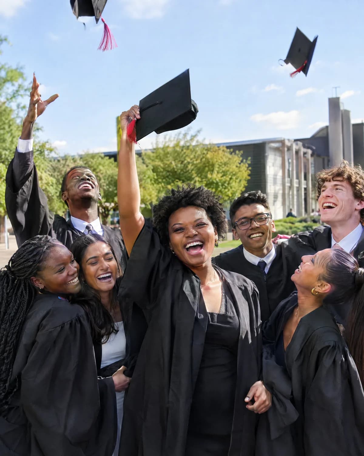 A group of graduates in gowns laughing and throwing their caps in the air